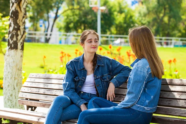 Två vackra flickvänner pratar i en Park sitter på en ben — Stockfoto