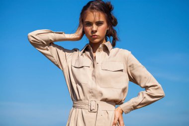 Bej elbiseli güzel esmer kız arkaya karşı poz