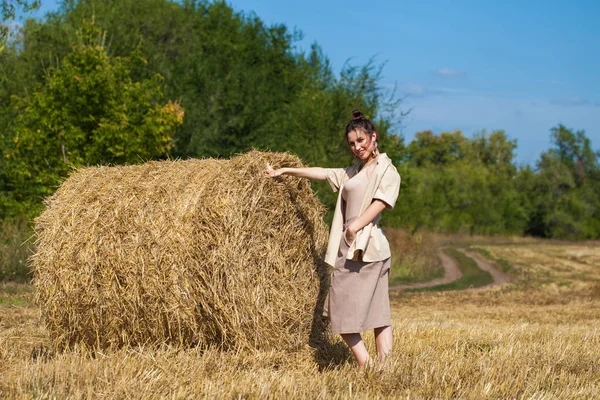 Vacker flicka i en beige kostym poserar på en bakgrund av haystac — Stockfoto