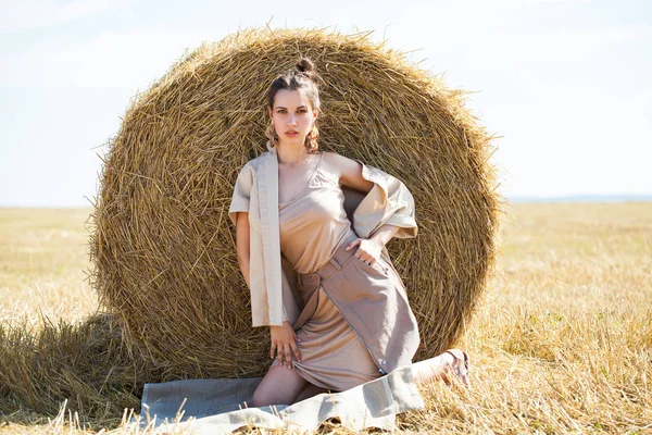 Beautiful girl in a beige suit posing on a background of haystac — Stock Photo, Image