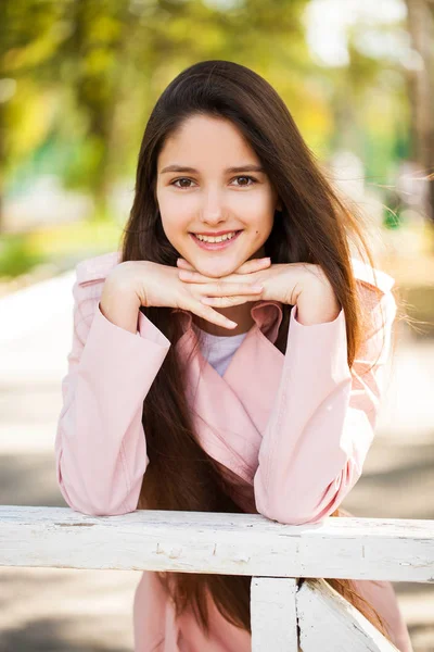Porträt eines jungen brünetten Mädchens in rosa Mantel auf einem Hintergrund o — Stockfoto