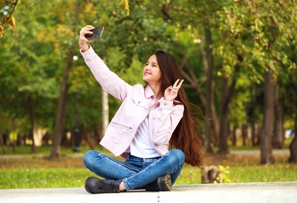 ブルネットの女の子は座っている間、携帯電話で自分自身を撮影 — ストック写真