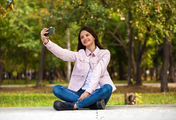 Brunette girl photographs herself on a cell phone while sitting — Stock Photo, Image