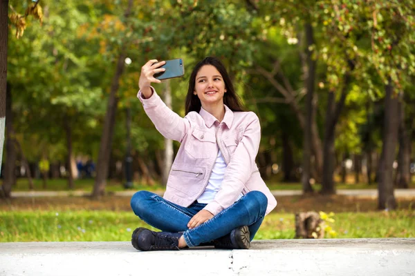 Brunette girl photographs herself on a cell phone while sitting — Stock Photo, Image