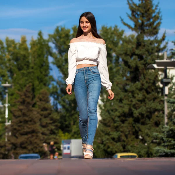 Jovem bela mulher morena em jeans e blusa branca andando — Fotografia de Stock