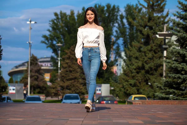 Joven hermosa morena mujer en jeans y blusa blanca caminando —  Fotos de Stock