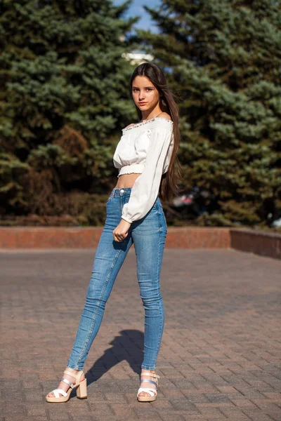 Bella ragazza bruna elegante in jeans blu e camicetta bianca — Foto Stock