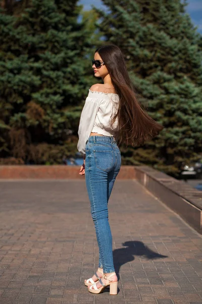 Bella ragazza bruna elegante in jeans blu e camicetta bianca — Foto Stock