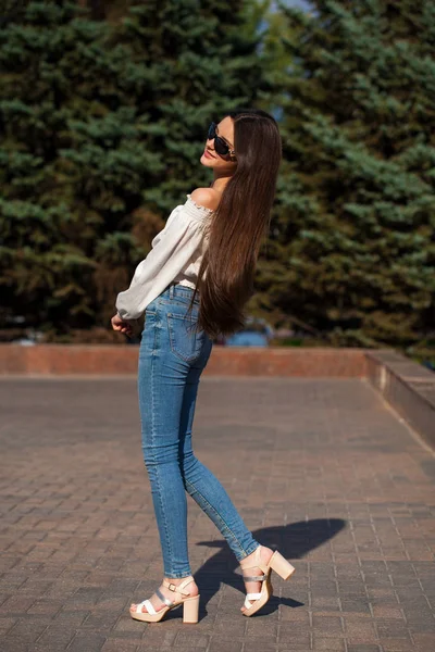 Ładna stylowa brunetka dziewczyna w niebieskie dżinsy i biała bluzka — Zdjęcie stockowe