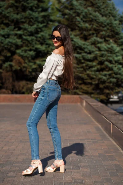 Bella ragazza bruna elegante in jeans blu e camicetta bianca — Foto Stock
