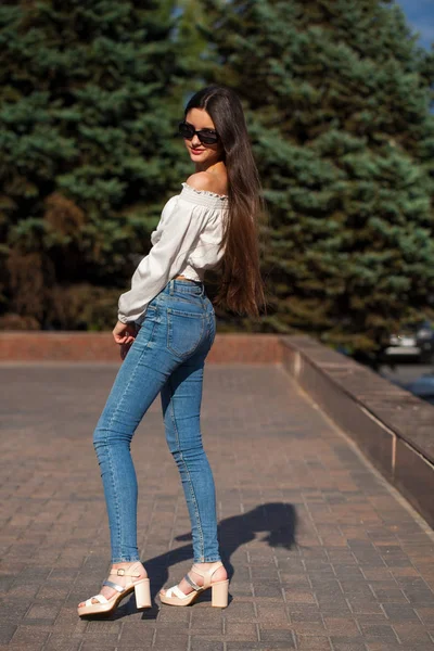 Ziemlich stylisches brünettes Mädchen in blauen Jeans und weißer Bluse — Stockfoto