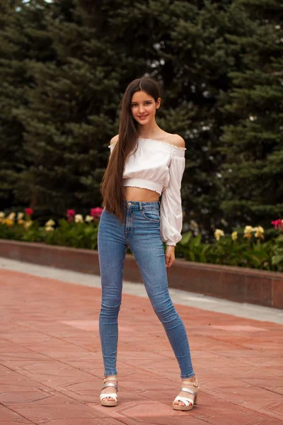 Bella ragazza bruna elegante in jeans blu e camicetta bianca — Foto Stock