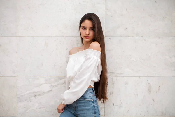 Menina bonita nova em um fundo de uma parede de mármore branco — Fotografia de Stock