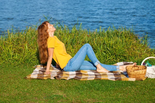 Młoda Ruda kobieta odpoczywa na trawniku w pobliżu jeziora — Zdjęcie stockowe