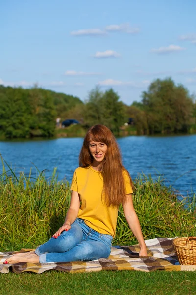 Mujer pelirroja joven descansando en el césped cerca del lago — Foto de Stock