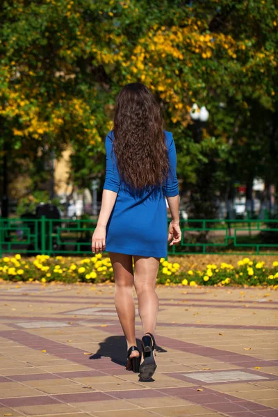 Молодая красивая женщина в темно-синем платье идет по летней улице — стоковое фото