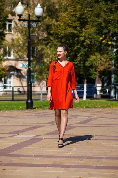 Молодая красивая модель в красном платье прогулка по летней улице — стоковое фото