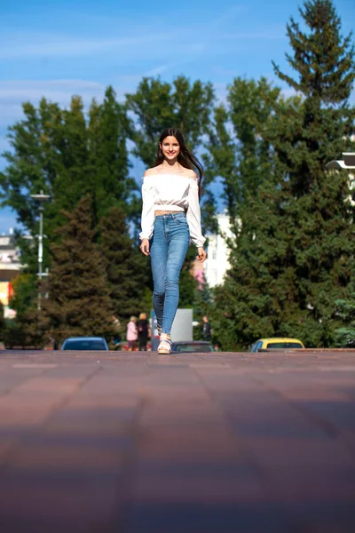 Jonge mooie brunette vrouw in jeans en witte blouse wandelen — Stockfoto