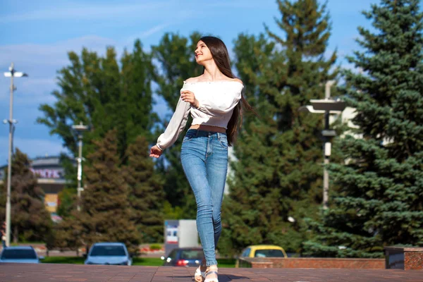 Νέα όμορφη μελαχρινή γυναίκα με τζιν και λευκή μπλούζα με τα πόδια — Φωτογραφία Αρχείου