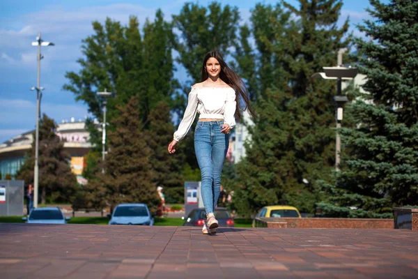 Young beautiful brunette woman in jeans and white blouse walking — Stock Photo, Image