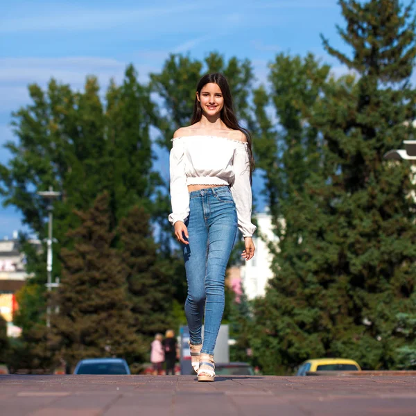 Jovem bela mulher morena em jeans e blusa branca andando — Fotografia de Stock