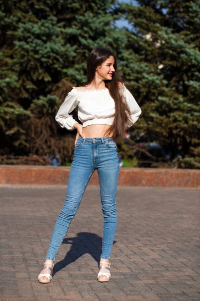 Bella ragazza bruna elegante in jeans blu e camicetta bianca — Foto Stock