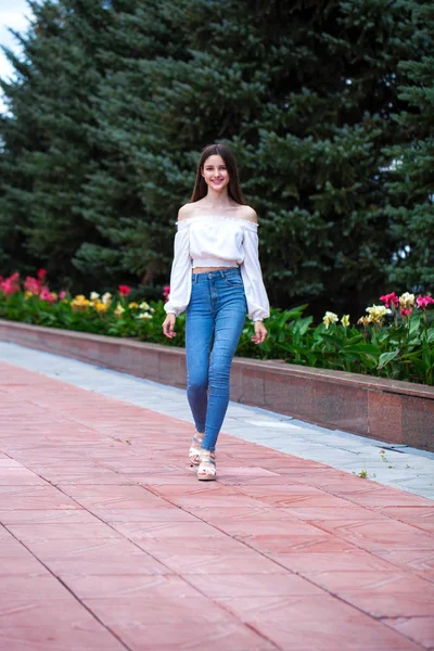 Giovane bella donna bruna in jeans e camicetta bianca a piedi — Foto Stock
