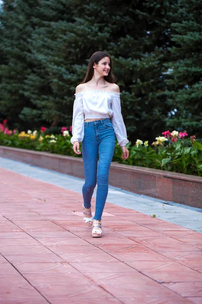 Joven hermosa morena mujer en jeans y blusa blanca caminando — Foto de Stock