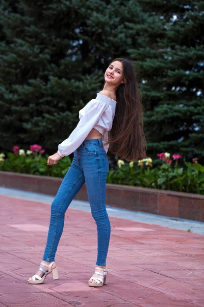 Bella ragazza bruna elegante in jeans blu e camicetta bianca — Foto Stock