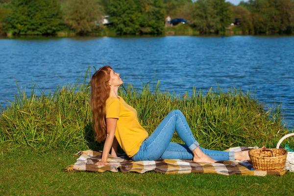 Młoda Ruda kobieta odpoczywa na trawniku w pobliżu jeziora — Zdjęcie stockowe