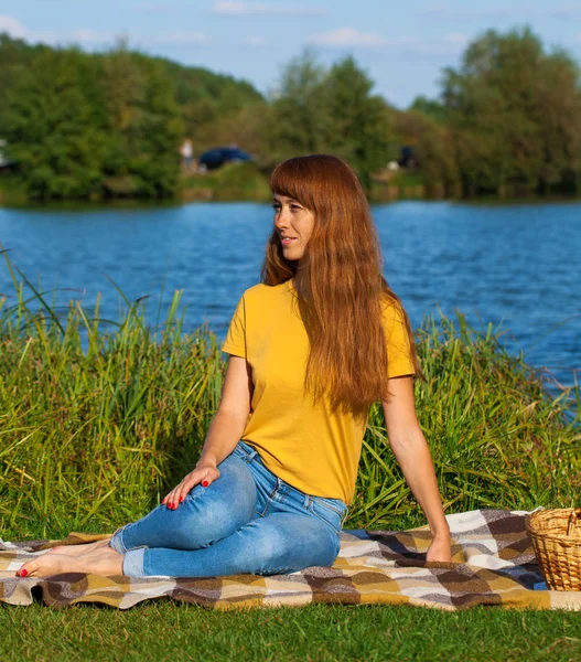 湖の近くの芝生の上で休んでいる若い赤毛の女性 — ストック写真