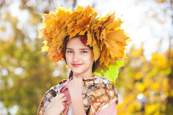 Glückliche junge schöne Mädchen mit einem Kranz aus Ahornblättern in autu — Stockfoto