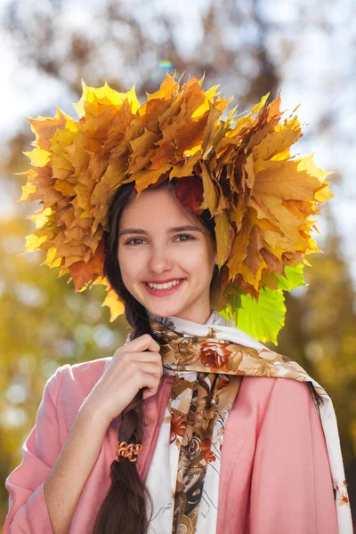Ευτυχισμένο νεαρό όμορφο κορίτσι με ένα στεφάνι από φύλλα σφενδάμου σε autu — Φωτογραφία Αρχείου