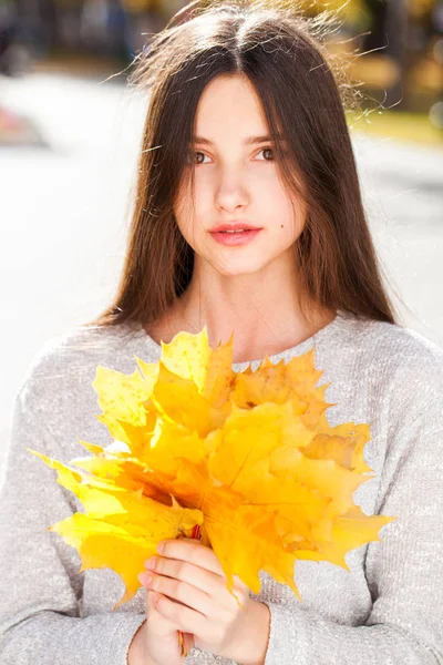 Egy fiatal lány portréja sárga juharfalevéllel. — Stock Fotó