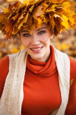 Akçaağaç yapraklarından çelengi olan genç ve güzel bir kadın au pozu veriyor.