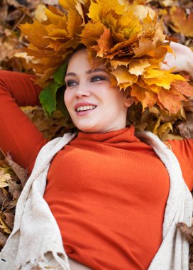 Akçaağaç yapraklarından çelengi olan genç ve güzel bir kadın au pozu veriyor.
