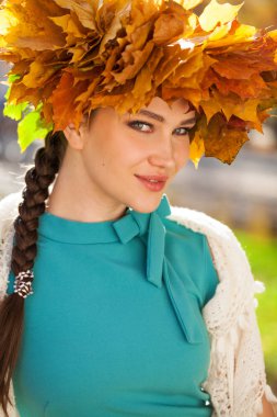 Akçaağaç yapraklarından çelengi olan genç ve güzel bir kadın au pozu veriyor.