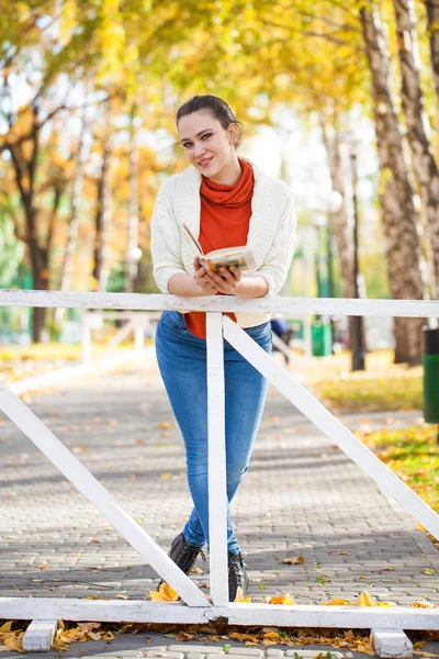 Mladá krásná žena s knihou v podzimním parku — Stock fotografie