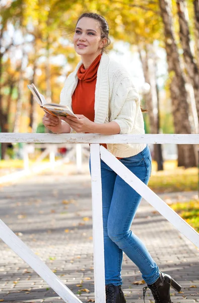 Giovane bella donna che legge un libro nel parco autunnale — Foto Stock