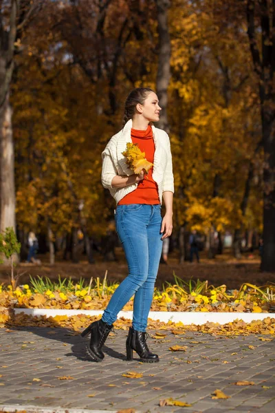 Sonbahar parkında poz veren kot pantolonlu güzel bir kadın. — Stok fotoğraf