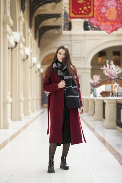 Hermosa chica con estilo en un abrigo largo de color burdeos, tienda interior —  Fotos de Stock