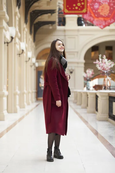 Vacker flicka i stilfull i en lång vinröd kappa, inomhus shop — Stockfoto