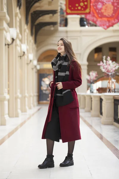 A szép lány a stílusos egy hosszú bordó kabátot, fedett shop — Stock Fotó