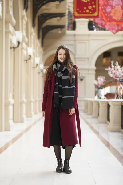 Beautiful girl in stylish in a long burgundy coat, indoor shop — Stock Photo, Image