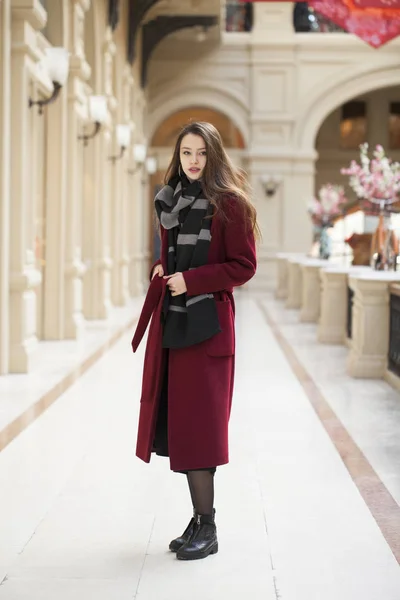 Krásná dívka ve stylové v dlouhé vínové kabátě, vnitřní obchod — Stock fotografie
