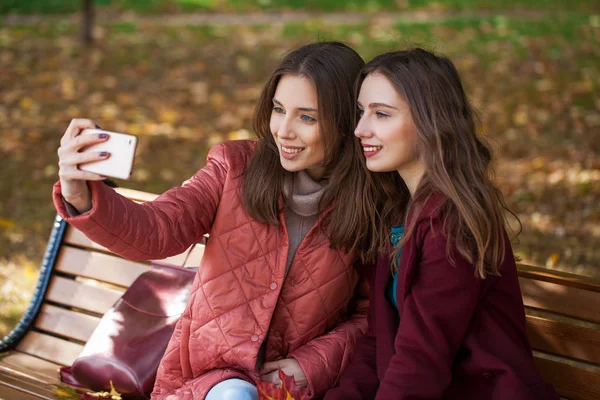 Dos hermosas chicas descansando en un banco en el parque de otoño — Foto de Stock