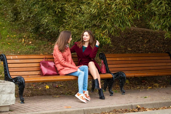 Two beautiful girls resting on a bench in the autumn park — Stock Photo, Image