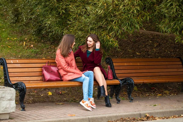 Dwie piękne dziewczyny odpoczywające na ławce w jesiennym parku — Zdjęcie stockowe