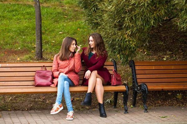 两个漂亮的姑娘在秋天公园的长椅上休息 — 图库照片