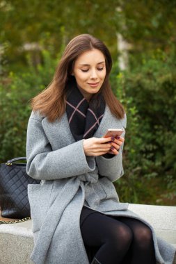 Gri paltolu güzel bir kadın bir mesaj yazıyor. 